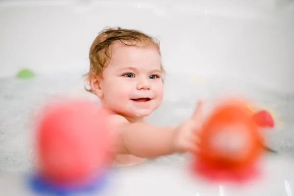 Schattig schattig baby meisje neemt schuimig bad in bad. Peuter spelen met bad rubber speelgoed. Mooi kind hebben plezier met kleurrijke kauwgom speelgoed en schuim bellen — Stockfoto