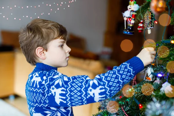 Kleiner Junge baut Weihnachtsschmuck vom Weihnachtsbaum ab. Familie nach dem Fest Baum entfernen und entsorgen. Jungen in festlicher Kleidung mit Rentieren. — Stockfoto