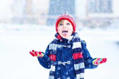 Renkli elbiseli komik küçük çocuk şiddetli kar yağışı sırasında dışarıda oynuyor.