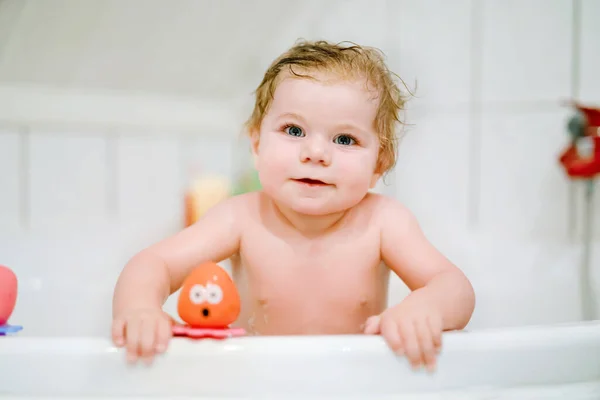 Linda menina adorável tomando banho espumoso na banheira. Criança brincando com brinquedos de borracha de banho. Criança bonita se divertindo com brinquedos coloridos de goma e bolhas de espuma — Fotografia de Stock