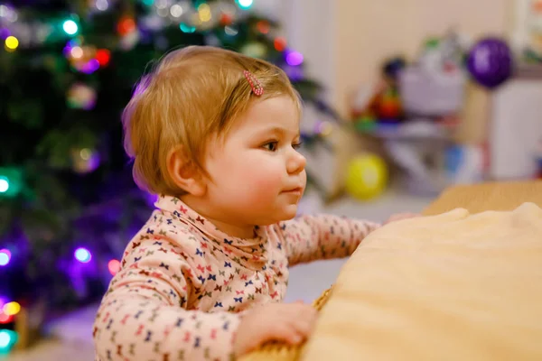 Retrato de pequena menina bonito aprendendo andando e de pé. com árvore de Chrismas e luzes no fundo. Menina da criança adorável em casa. Bela criança bebê em roupas casuais — Fotografia de Stock