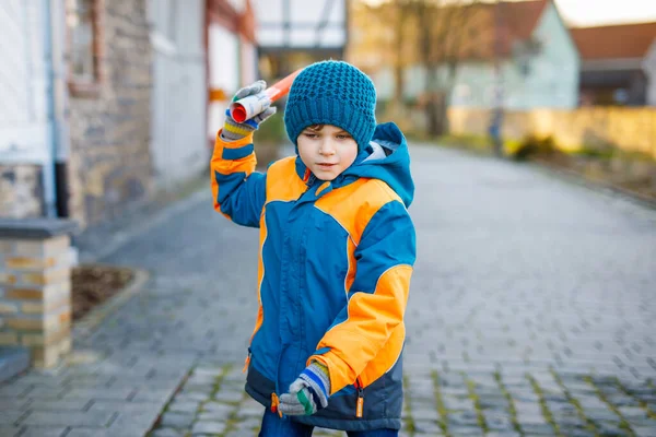 Chłopiec z podstawówki, idący do szkoły w mroźny zimowy dzień. Szczęśliwe dziecko bawiące się na ulicy. Student z plecakiem w kolorowe ubrania zimowe trzyma rzeczy do projektu — Zdjęcie stockowe