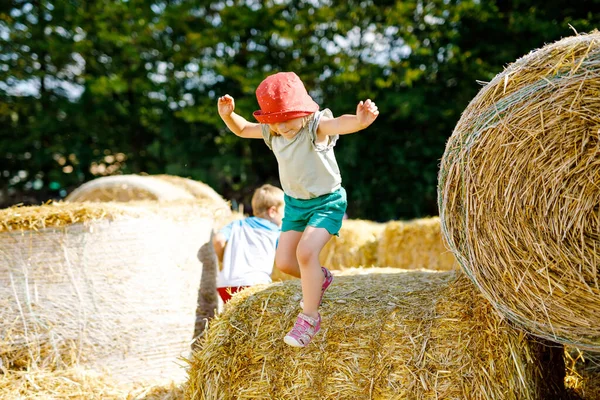 Little toddler girl having fun with running and jumping on hay stack or bale. Funny happy healthy child playing with straw. Active outdoors leisure with children on warm summer day. Kids and nature — Stock Photo, Image