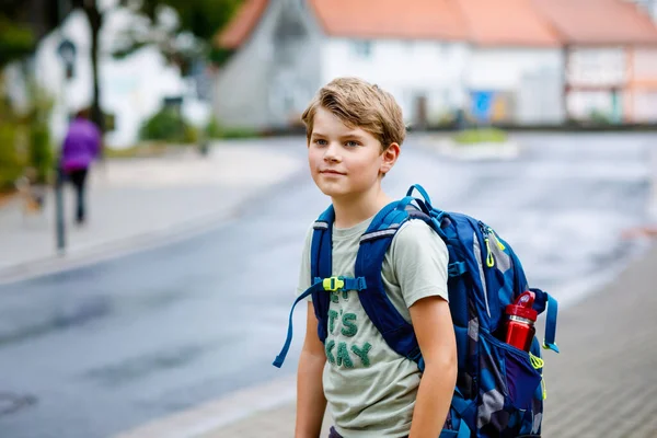 Rapazinho feliz com mochila ou mochila. Um estudante a caminho do liceu ou do liceu. Criança adorável saudável ao ar livre na rua, em dia chuvoso. De volta à escola. — Fotografia de Stock