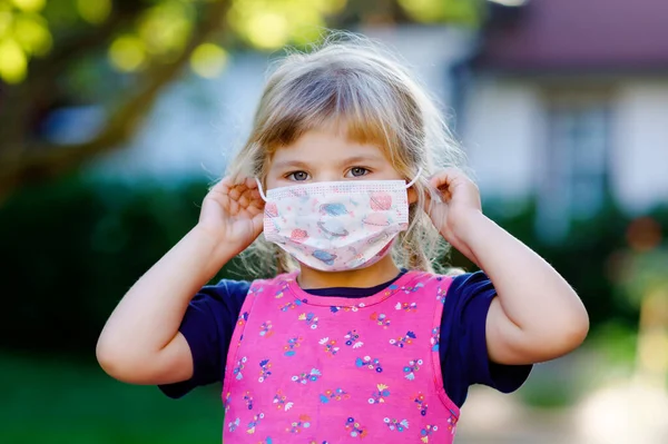 Pequeña niña en máscara médica como protección contra la enfermedad de cuarentena por coronavirus pandémico. Lindo uso de niños y poner equipo de protección como lucha contra covid 19. — Foto de Stock