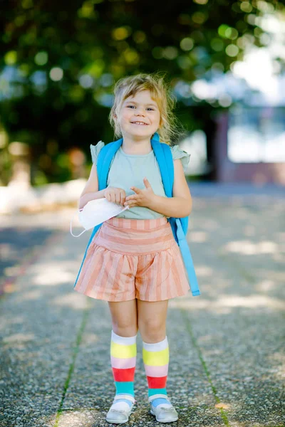 놀이방가는 첫날, 코로나 코비 드 바이러스에 대항하는 의료용 마스크를 쓰고 걸음마하는 여자아이. 보육원이나 유치원으로 걸어가는 건강하고 아름다운 아기. 가방을 든 행복 한 아이 — 스톡 사진