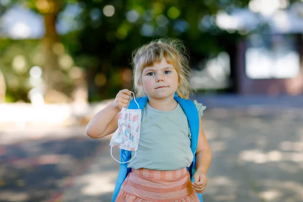 Egy kisbaba lány az első napján, aki orvosi maszkot visel a Corona Covid vírus ellen. Egészséges gyönyörű baba sétál óvodába és óvodába. Boldog gyermek hátizsákkal — Stock Fotó
