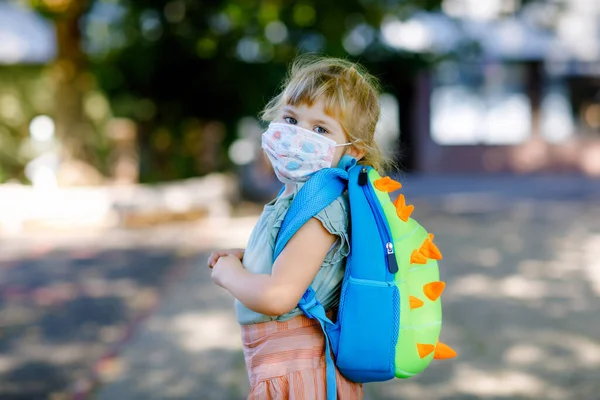 Menina criança em seu primeiro dia a caminho de playschool com máscara médica contra o vírus corona covid. Bebê bonito saudável caminhando para pré-escola e jardim de infância. Criança feliz com mochila — Fotografia de Stock