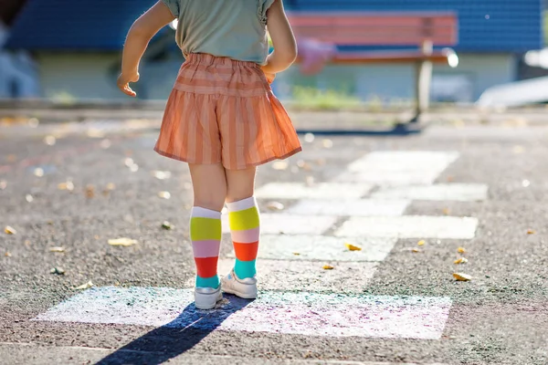 Closeup of leggs of little toddler girl playing hopscotch game drawn with colorful chalks on asphalt. Little active child jumping on playground outdoors on a sunny day. Summer activities for children. — Stock Photo, Image