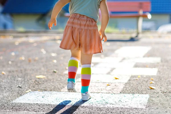 Nahaufnahme der Beine von kleinen Mädchen spielen Hopscotch-Spiel mit bunten Kreiden auf Asphalt gezeichnet. Kleines aktives Kind, das an einem sonnigen Tag auf dem Spielplatz im Freien springt. Sommeraktivitäten für Kinder. — Stockfoto