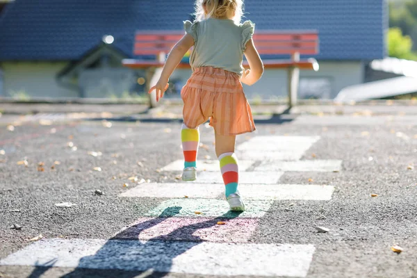 Close-up de pernas de menina pequena criança jogando hopscotch jogo desenhado com giz coloridos no asfalto. Pequena criança ativa pulando no playground ao ar livre em um dia ensolarado. Atividades de verão para crianças. — Fotografia de Stock