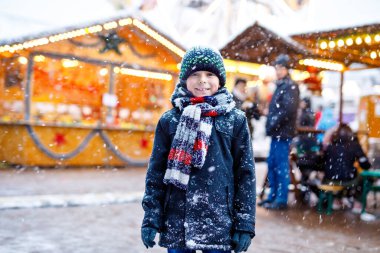 Küçük şirin çocuk şiddetli kar yağışında geleneksel Alman Noel pazarında eğleniyor. Mutlu çocuk Almanya, Münih 'te geleneksel aile pazarının tadını çıkarıyor. Renkli giysiler içinde gülen çocuk.