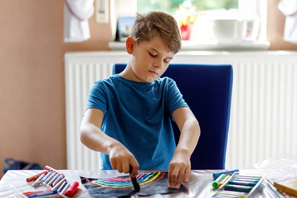 Little school kid boy paint rainbow with different stick colors on black background during pandemic coronavirus quarantine disease. Children painting rainbows around the world. Happy child indoors — Stock Photo, Image