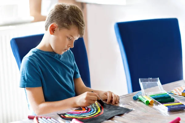 Little school kid boy måla regnbåge med olika pinne färger på svart bakgrund under pandemisk coronavirus karantän sjukdom. Barn målar regnbågar runt om i världen. Glada barn inomhus — Stockfoto