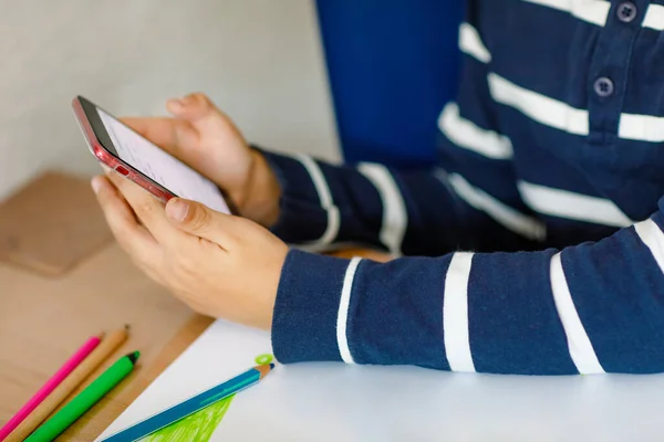 Großaufnahme eines Schuljungen, der während der Quarantäne Hausaufgaben vor der Coronapandemie macht. Gesundes Kinderschreiben mit Stift und Lernen per Smartphone. Heimschulkonzept — Stockfoto