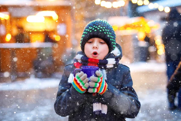 Pequeno menino bonito bebendo crianças quentes soco ou chocolate no mercado de Natal alemão. Criança feliz no mercado familiar tradicional na Alemanha, menino rindo em roupas coloridas de inverno — Fotografia de Stock