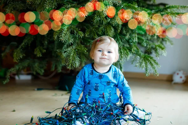 可爱的女婴从圣诞树上取下节日装饰品.拿着轻便花环的孩子。庆祝活动结束后，家人移走和处理树木 — 图库照片