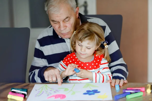 Roztomilé batolátko a pohledný seniorský obraz dědy s barevnými plstěnými pery a tužkami doma. Vnouče a muž baví spolu, tvůrčí rodina. — Stock fotografie