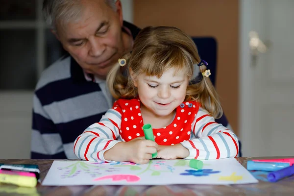 Χαριτωμένο μικρό κοριτσάκι και όμορφος ανώτερος παππούς ζωγραφική με πολύχρωμα στυλό τσόχα και μολύβια στο σπίτι. Εγγονός και άνθρωπος που διασκεδάζουν μαζί, δημιουργική οικογένεια. — Φωτογραφία Αρχείου