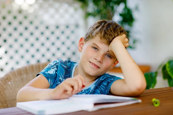 Niño de escuela feliz trabajador haciendo tarea durante el tiempo de cuarentena de la enfermedad pandémica de corona. Niño sano escribiendo con bolígrafo, quedándose en casa. Concepto de educación en el hogar — Foto de Stock