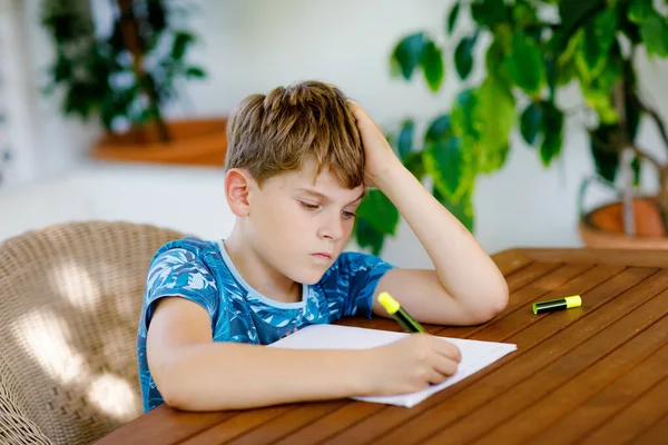 Niño de escuela feliz trabajador haciendo tarea durante el tiempo de cuarentena de la enfermedad pandémica de corona. Niño sano escribiendo con bolígrafo, quedándose en casa. Concepto de educación en el hogar — Foto de Stock