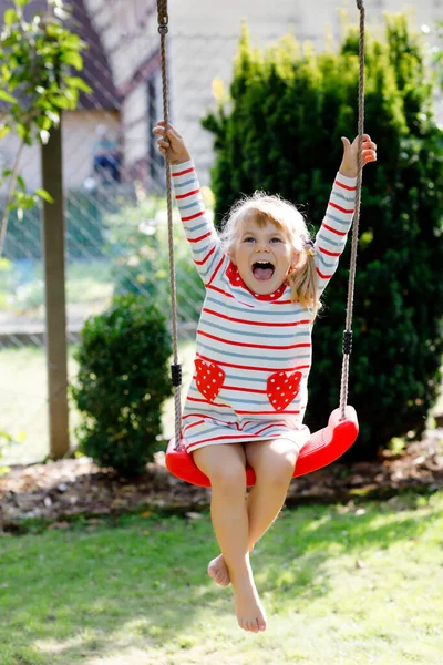 Küçük mutlu kız, salıncakta salıncakta sallanıyor. Güneşli bir bahar gününde ağaçların altında sallanan tatlı sağlıklı bir çocuk. Bebek gülüyor ve ağlıyor — Stok fotoğraf