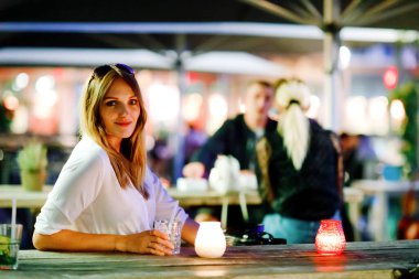 Genç bir kadın sıcak yaz gününde kafedeki terasta mojito kokteyli içiyor. Güzel bir iş kadını işten sonra restoranda sıcak bir akşam geçiriyor. Mutlu yalnız gülümseme bayan..