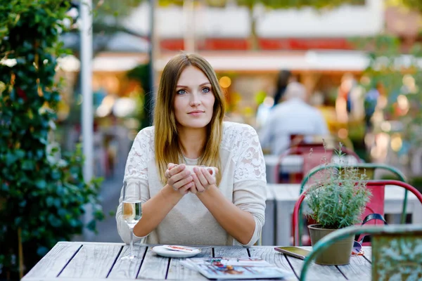 Młoda piękna kobieta pije cappuccino i filiżankę kawy i szklanego szampana czekając na przyjaciela i śniadanie. Szczęśliwa samotna kobieta w kawiarni lub restauracji na słoneczny letni dzień. — Zdjęcie stockowe