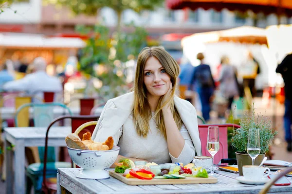 Mladá krásná žena pije kávu a mají snídani, zatímco čeká na přítele. Happy sám žena v venkovní kavárně nebo restauraci na slunné léto nebo na začátku podzimního dne. — Stock fotografie