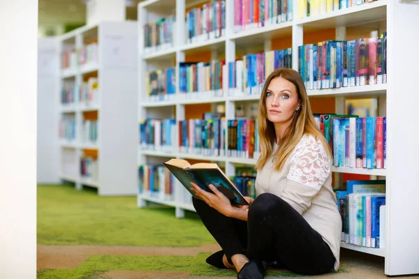 Young beautiful woman in public library, holding, reading and choosing books for leisure or education. Woman making research for college study — Stock Photo, Image