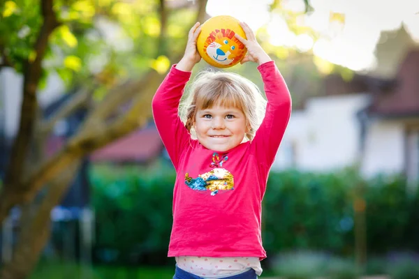 Pequeña adorable niña jugando con la pelota al aire libre. Feliz niño sonriente atrapando y lanzando, riendo y haciendo deportes. Ocio activo con niños y niños. —  Fotos de Stock