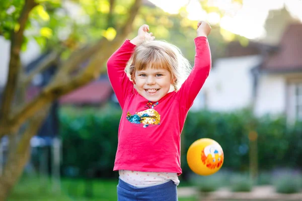 Dışarıda topla oynayan küçük sevimli bir kız. Gülümseyen çocuk yakalayıp fırlatıyor, gülüyor ve spor yapıyor. Çocuklar ve çocuklarla aktif eğlence.. — Stok fotoğraf