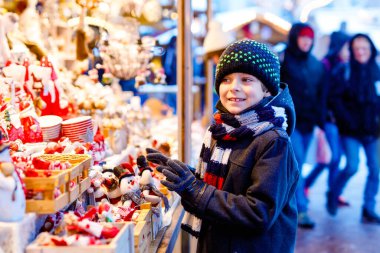 Noel pazarında dekorasyon seçen sevimli çocuk. Oyuncaklar için alışveriş yapan güzel bir çocuk ve ağaç için dekoratif süsler. Almanya 'da Xmas pazarı.