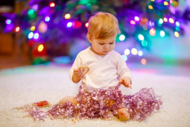 Sevimli bir kız bebek ellerinde renkli bir çelenk tutuyor. Noel ağacını aile ile süsleyen şenlikli elbiseli küçük bir çocuk. Weihnachten adlı geleneksel bayramın ilk kutlaması.