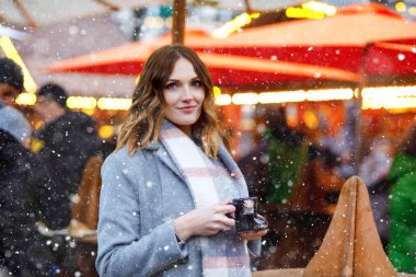 Güzel genç bir kadın sıcak punç içiyor, Alman Noel pazarında sıcak şarap içiyor. Kış kıyafetleri içinde mutlu bir kız. Arka planda ışıklar var. Berlin, Almanya 'da kış günü kar tatilinde..