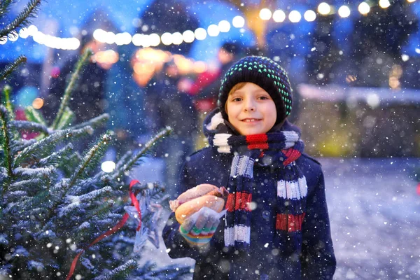 Pequeño niño lindo comiendo salchicha alemana y beber ponche niños calientes en el mercado de Navidad. Niño feliz en el mercado familiar tradicional en Alemania. Chico risueño en ropa de invierno colorida — Foto de Stock