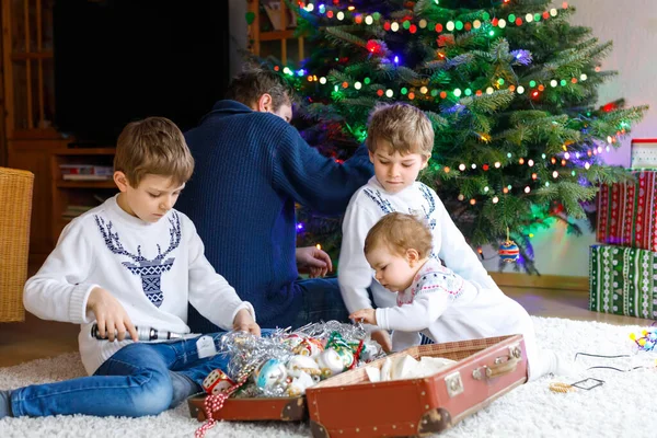 Zwei kleine Jungen und ein entzückendes Mädchen schmücken den Weihnachtsbaum mit altem Spielzeug und Bällen. Papa im Hintergrund — Stockfoto