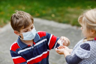 Liseli çocuk küçük kız kardeşine dezenfektanla el temizleme konusunda yardım ediyor. Kardeş ve tatlı küçük kız hijyen kurallarını öğreniyorlar. Coronavirus ve grip salgını sırasında aile. Covid virüs koruması.