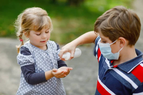 Niño de la escuela ayudando a la hermana pequeña a limpiarse las manos con aerosol desinfectante. Hermano y linda niña aprenden reglas de higiene. Familia durante el cierre del coronavirus y la gripe. Protección del virus covid. —  Fotos de Stock