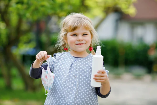 Niña pequeña con máscara médica como protección contra la enfermedad de cuarentena por coronavirus pandémico. Lindo niño sosteniendo la botella con desinfectante para limpiar las manos. equipo de protección contra el covidio — Foto de Stock