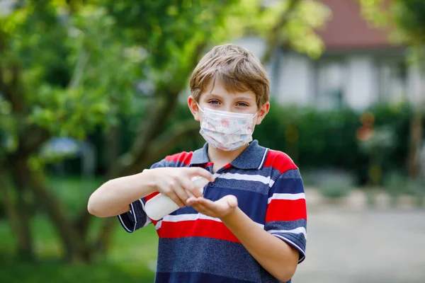 Niño escolar con máscara médica como protección contra la enfermedad de cuarentena por coronavirus pandémico. Botella para niños con desinfectante para la limpieza de manos. equipo de protección contra el covidio — Foto de Stock