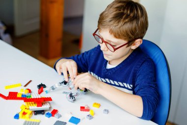 Gözlüklü küçük sarışın çocuk bir sürü renkli plastik blokla oynuyor. Sevimli okul çocuğu robot yaparak ve yaratarak eğleniyor. Yaratıcı eğlence modern teknik ve robotik.