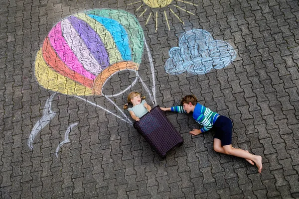 Menina pequena feliz e garoto voando em balão de ar quente pintado com giz colorido em cores do arco-íris no chão ou asfalto no verão. Dois filhos, irmãos a divertirem-se. Lazer criativo — Fotografia de Stock