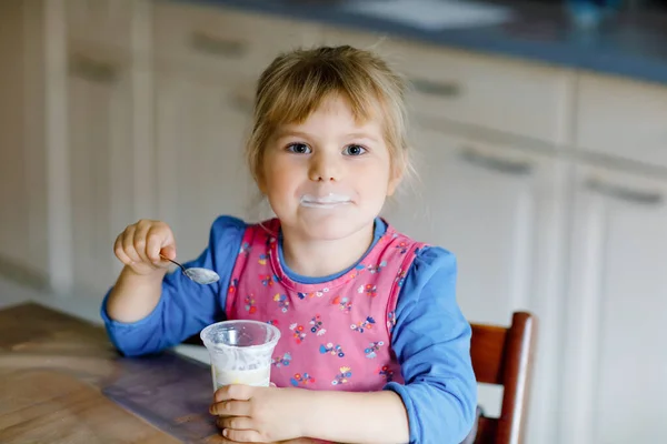 Mała dziewczynka je jogurt na śniadanie. Cute zdrowe dziecko siedzi w kuchni lub w przedszkolu i posiłek. — Zdjęcie stockowe