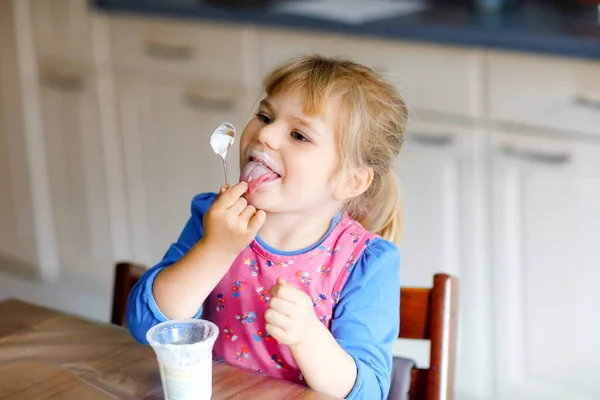 아침으로 요구르트를 먹는 어린 소녀. 부엌에 앉아 있거나 아기방에 있거나 식사를 하고 있는 건강 한 아기를 귀여워 한다. — 스톡 사진