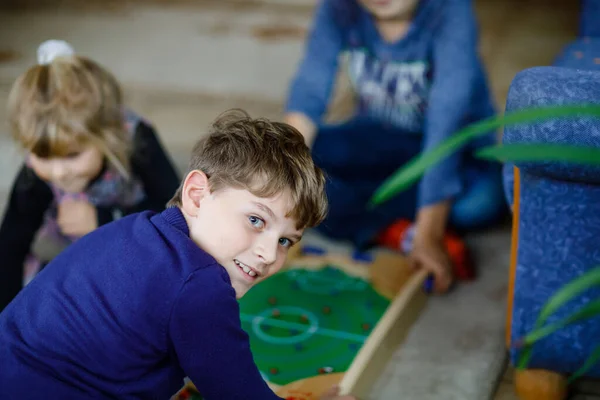 Twee gelukkige jongens die tafelvoetbal spelen met vrienden thuis. Glimlachend kind dat plezier heeft met boardvoetbal, binnen. Zuster op achtergrond — Stockfoto