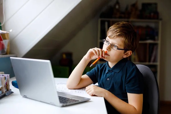 Garoto com óculos aprendendo em casa no laptop para a escola. Criança adorável fazendo lição de casa e usando notebook e gadgets modernos. Conceito de escola doméstica. — Fotografia de Stock