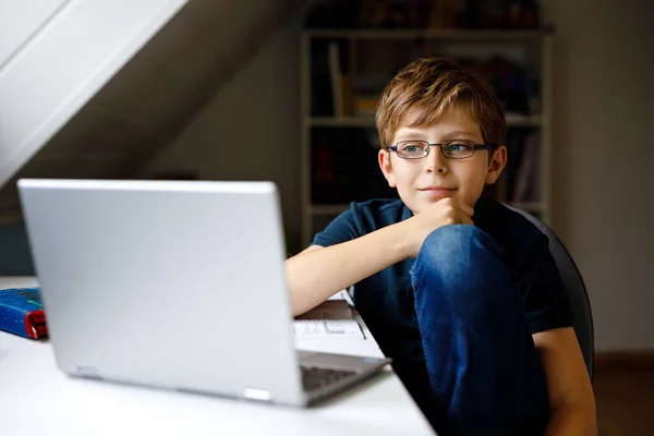 Мальчик в очках учится дома на ноутбуке для школы. Очаровательный ребенок делает домашнее задание и с помощью ноутбука и современных гаджетов. Концепция домашнего обучения. — стоковое фото