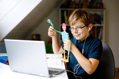 Gözlüklü çocuk evde okulda laptopta öğreniyor. Ev ödevi yapan, defter ve modern aletler kullanan sevimli bir çocuk. Evde eğitim kavramı.