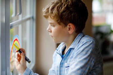 Salgın koronavirüs karantinası sırasında renkli pencere renginde pijama giyen sevimli okul çocuğu. Dünyanın dört bir yanında çocuklar gökkuşağı çiziyor..